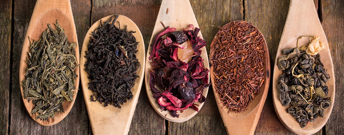 Différents types de thé disposés dans des cuillères en bois : thé vert, thé noir, thé jasmin