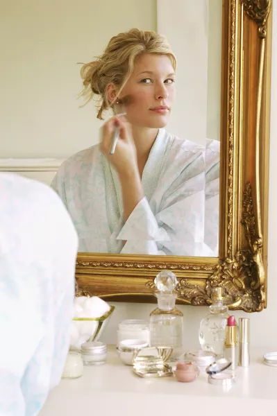 Une femme se maquille devant un miroir. 