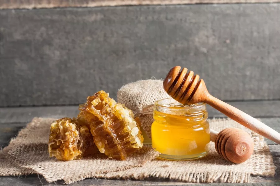 Un bocal de miel, une cuillère à miel et des alvéoles disposés sur de la toile de jute
