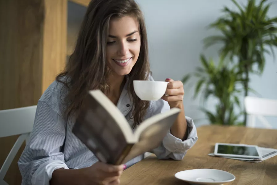 Une femme s’accorde un moment de lecture en buvant un café.