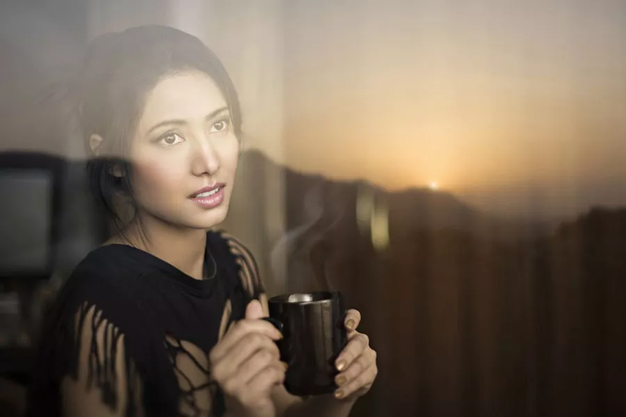 Une femme déguste un café en regardant par une fenêtre
