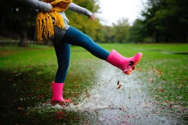 Une femme vêtue de bottes de pluie saute dans des flaques d’eau
