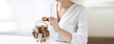 Une femme mange des cookies rangés dans un bocal