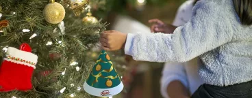 Une petite fille accroche un sapin de noel Pépito Emochoco dans un arbre de Noël