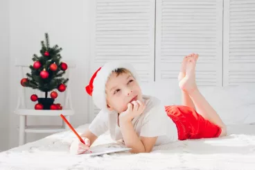 Un petit garçon allongé sur un lit écrit au Père Noël 
