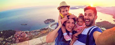 Des parents avec leurs deux enfants qui se prennent en selfie, en vacances, devant un paysage de rêve