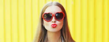 Une jeune femme avec des lunettes rouges en forme de cœur qui fait un bisou