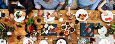 Un groupe de convives attablés autour d’une table en bois garnie de produits culinaires