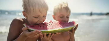 enfants à la plage mangeant une pastèque
