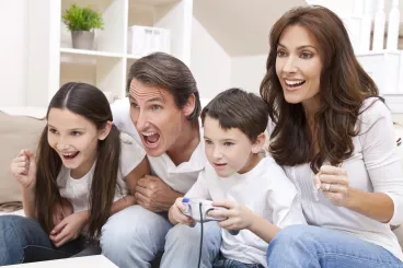 Jeux-vidéos en famille : et si vous sautiez le pas ? Famille s’amusant et partageant un moment convivial en jouant aux jeux-vidéos