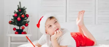 Un petit garçon allongé sur un lit écrit au Père Noël 