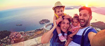 Des parents avec leurs deux enfants qui se prennent en selfie, en vacances, devant un paysage de rêve