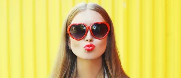 Une jeune femme avec des lunettes rouges en forme de cœur qui fait un bisou