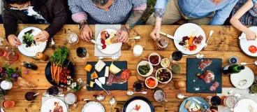 Un groupe de convives attablés autour d’une table en bois garnie de produits culinaires