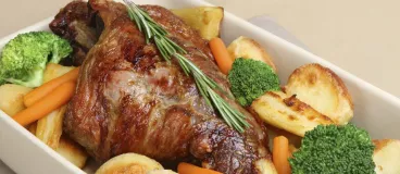 Gigot d’agneau servi à table dans son plat et ses légumes