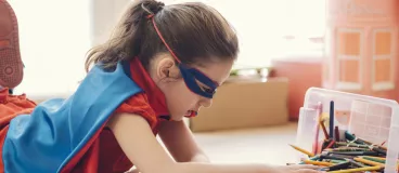 Une petite fille habillée en super héros fait des coloriages