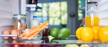 Jeune femme tenant la porte d’un frigo presque vide 