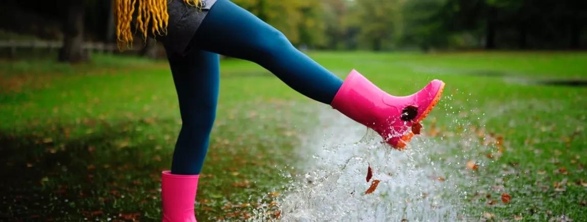 DIY d'automne : pour des bottes qui vous bottent ! Une femme vêtue de bottes de pluie saute dans des flaques d’eau