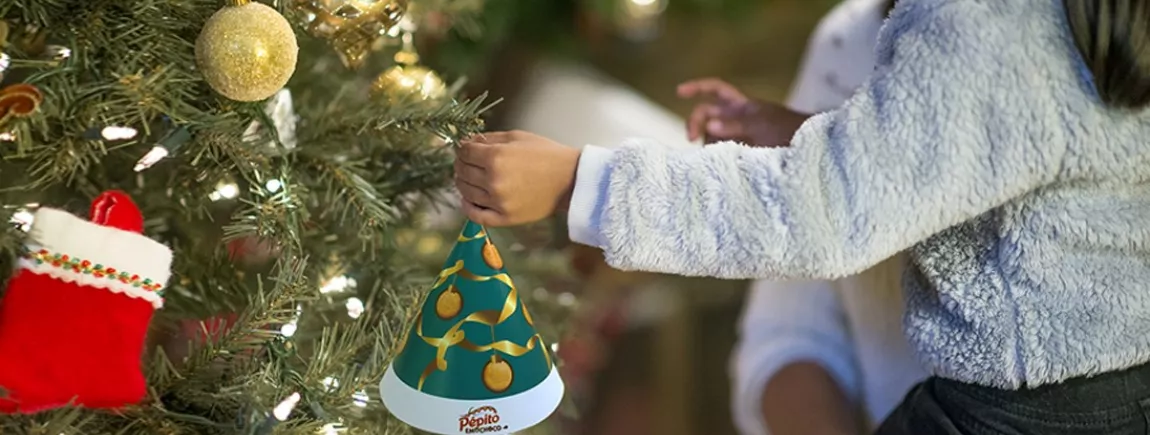 Une petite fille accroche un sapin de noel Pépito Emochoco dans un arbre de Noël