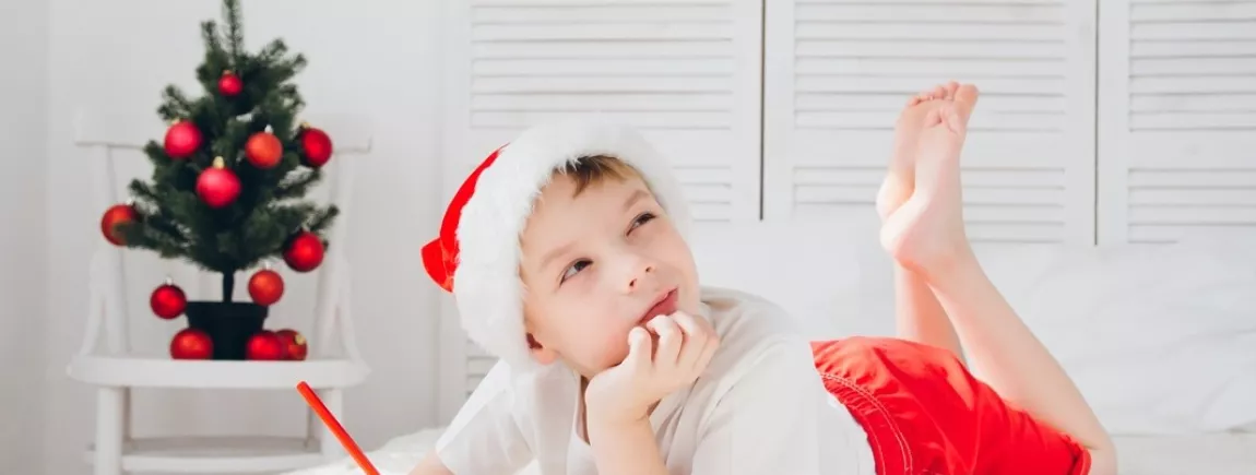 Un petit garçon allongé sur un lit écrit au Père Noël 