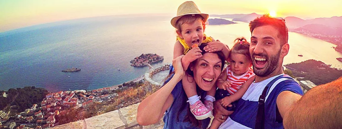 Des parents avec leurs deux enfants qui se prennent en selfie, en vacances, devant un paysage de rêve
