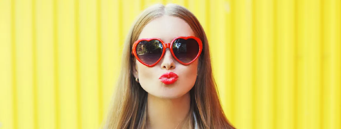 Une jeune femme avec des lunettes rouges en forme de cœur qui fait un bisou