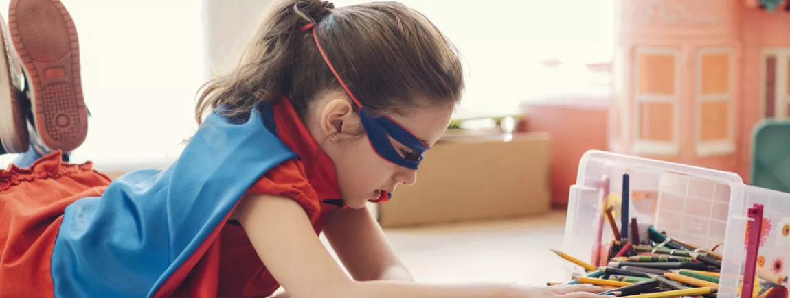 Une petite fille habillée en super héros fait des coloriages