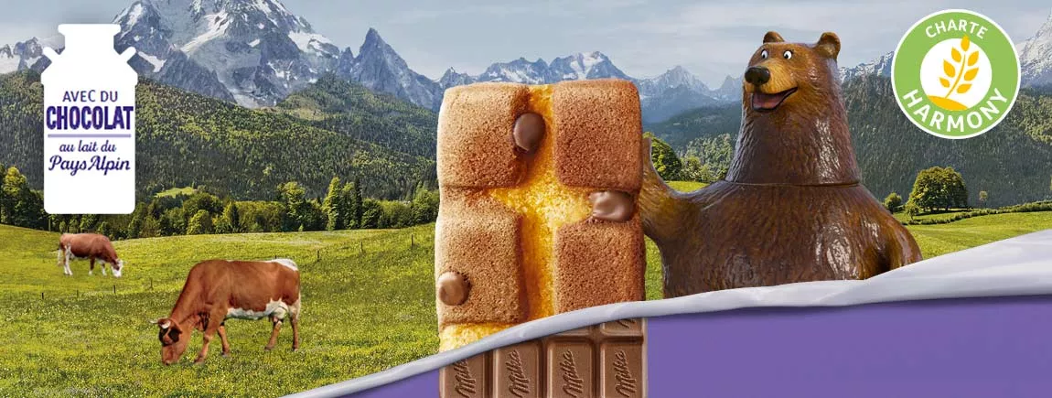 Découvrez les secrets de vos bons biscuits Milka® Un ours tient une madeleine chocolatée Milka devant un fond Alpin