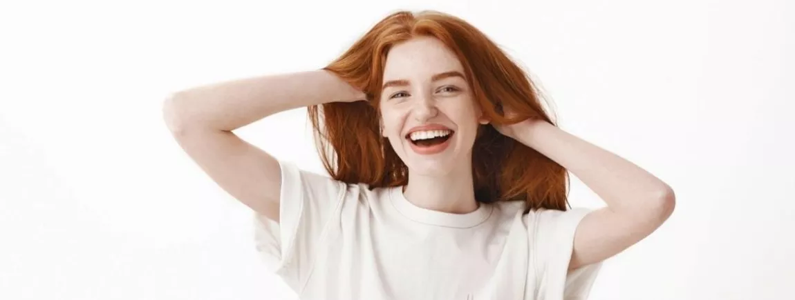 Comment apporter de l’éclat aux cheveux ternes ? Cheveux roux. Soin des cheveux. Jeune femme souriante. Fond blanc. Cheveux longs. Cheveux brillants.