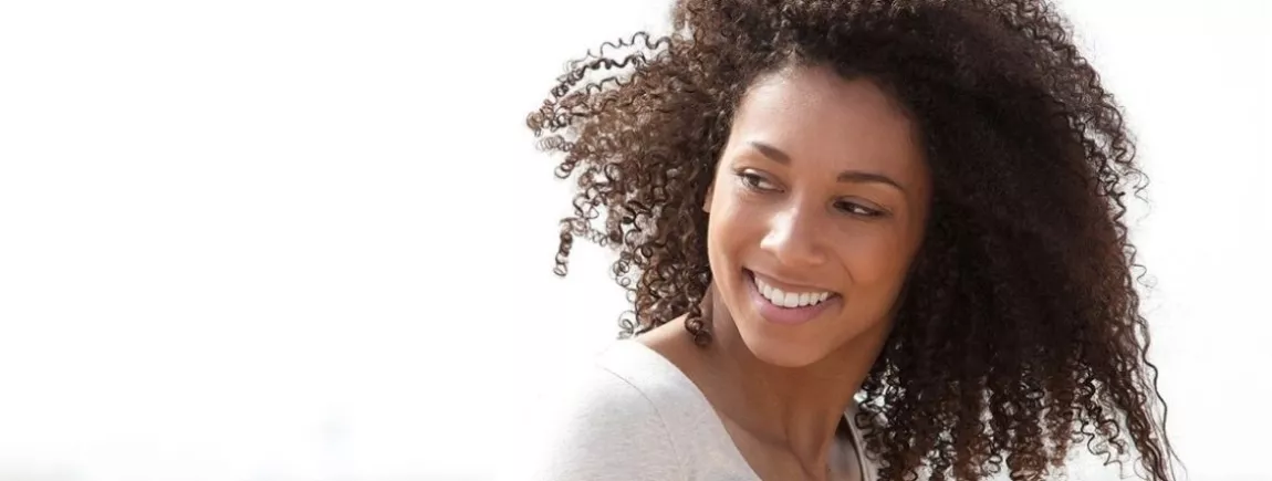 Comment prendre soin des cheveux bouclés et frisés ? Cheveux bruns. Soin des cheveux. Jeune femme souriante. Cheveux longs. Cheveux brillants.Cheveux crépus.